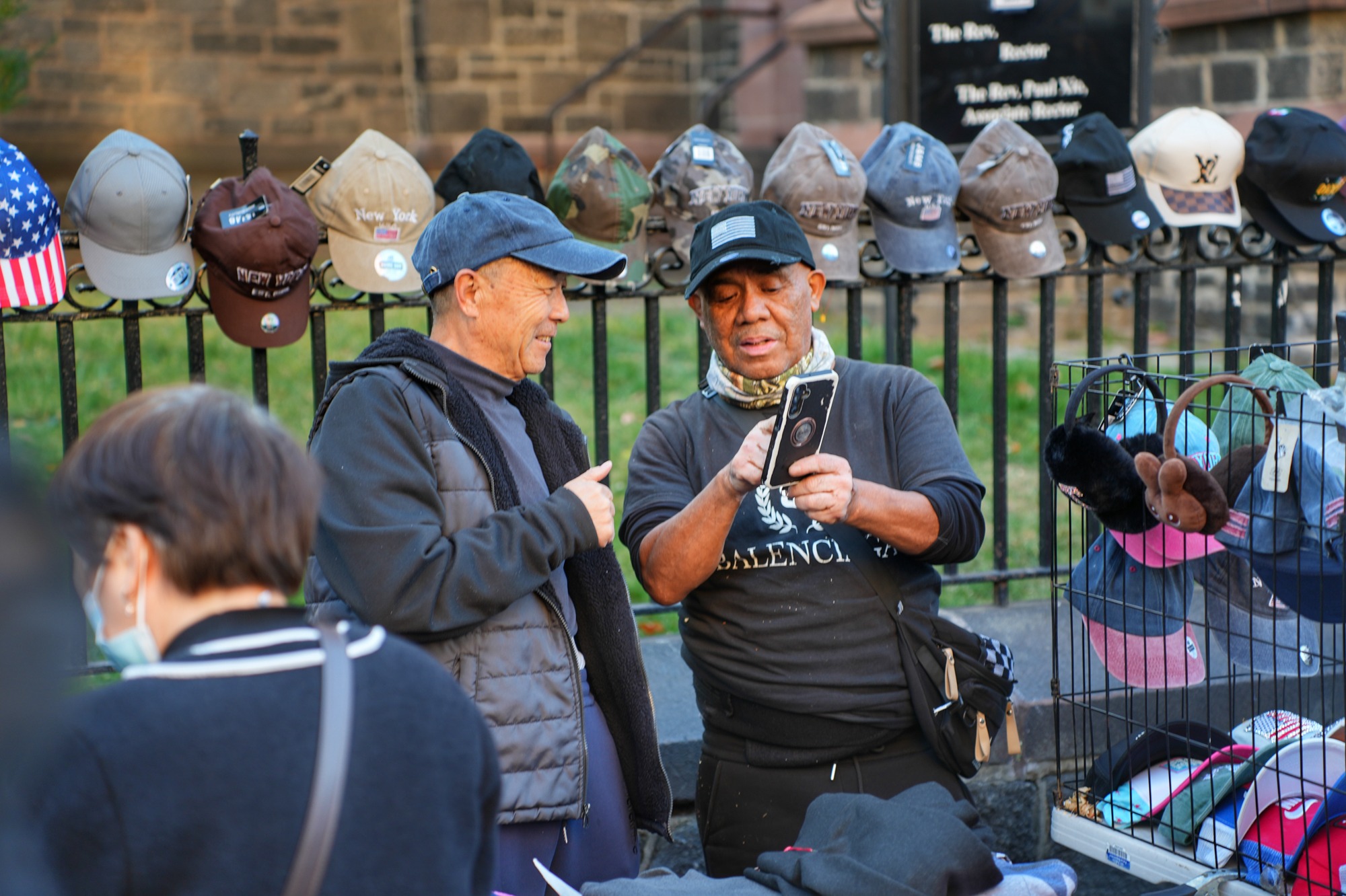 Two street vendors look at a phone beside a hat display outside a church. Nov. 8, 2025.