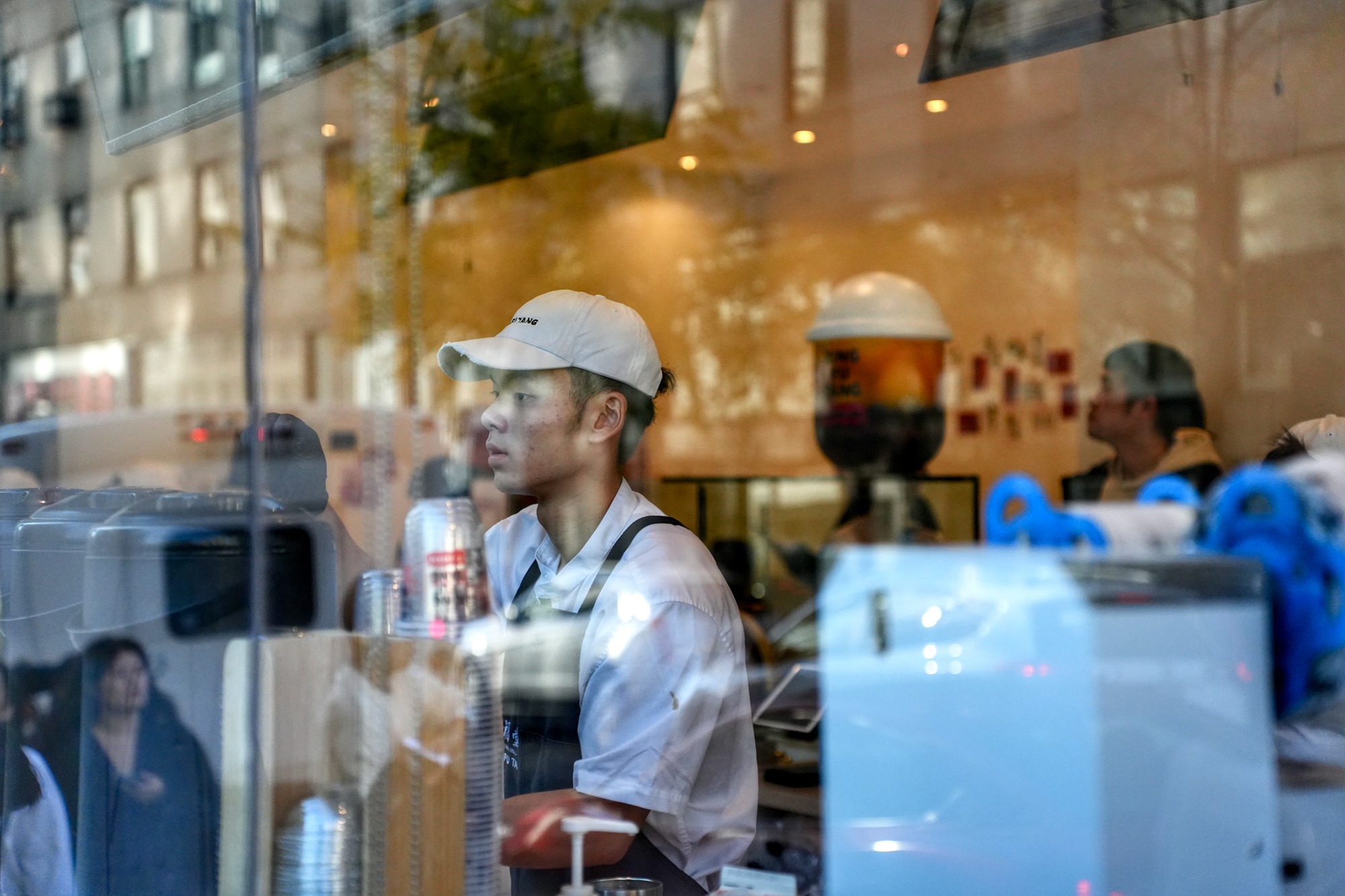 A milk-tea worker prepares drinks while looking through the storefront window. Nov. 8, 2025.