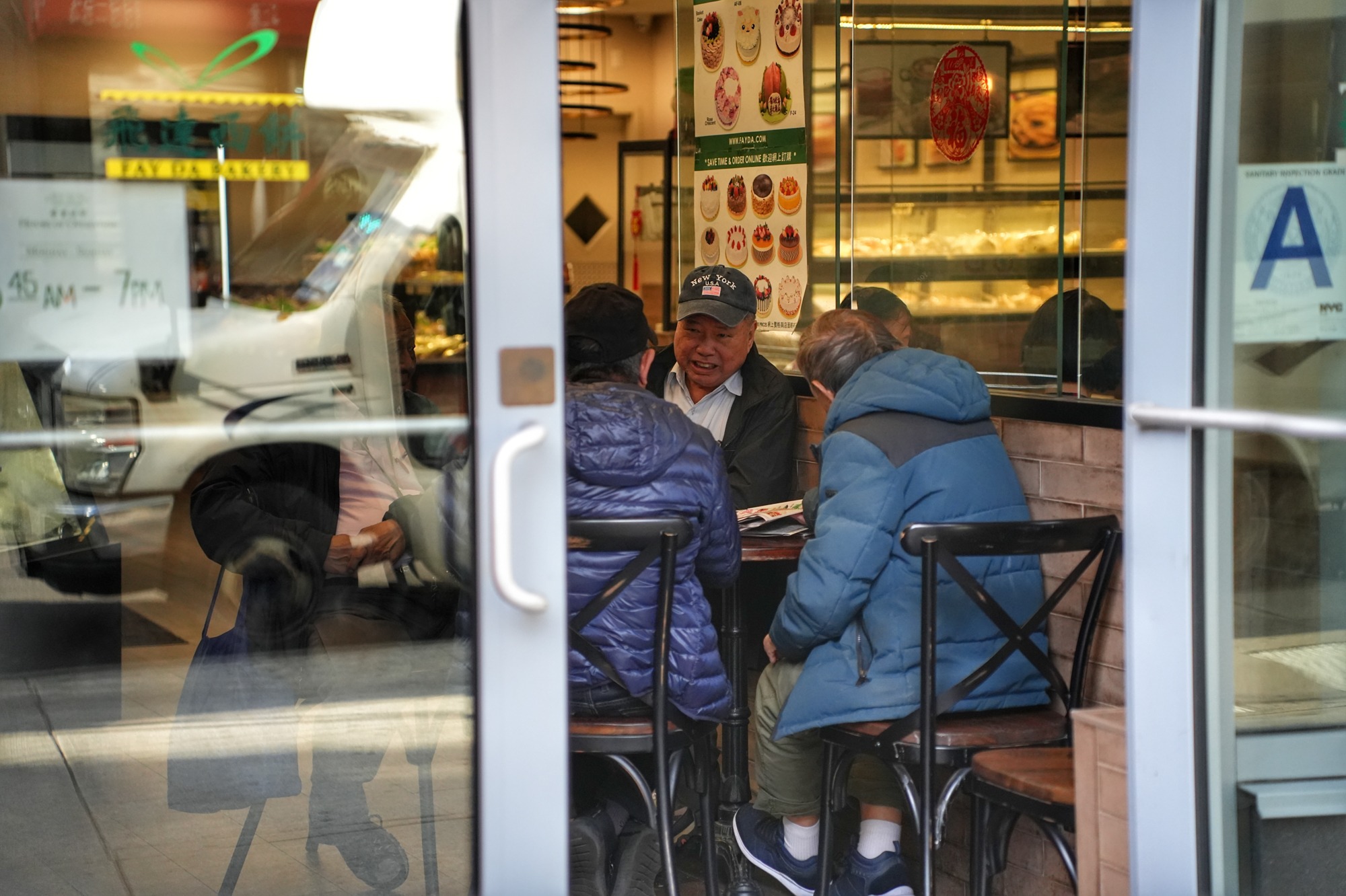 Diners gather around a table inside a Flushing restaurant, seen through the storefront window. Nov. 8, 2025.