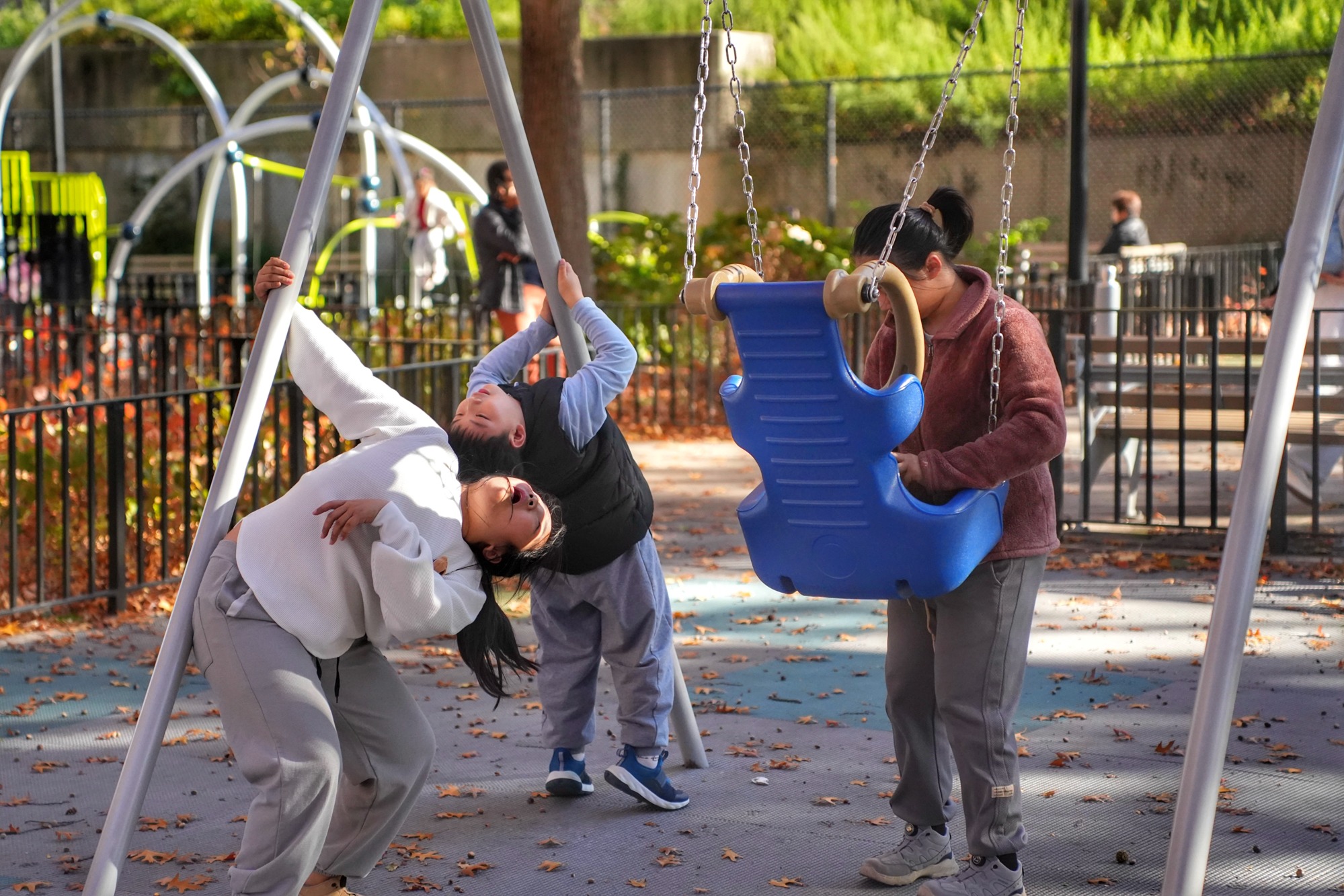A woman and two children share a swing on a mild autumn afternoon. Nov. 8, 2025.