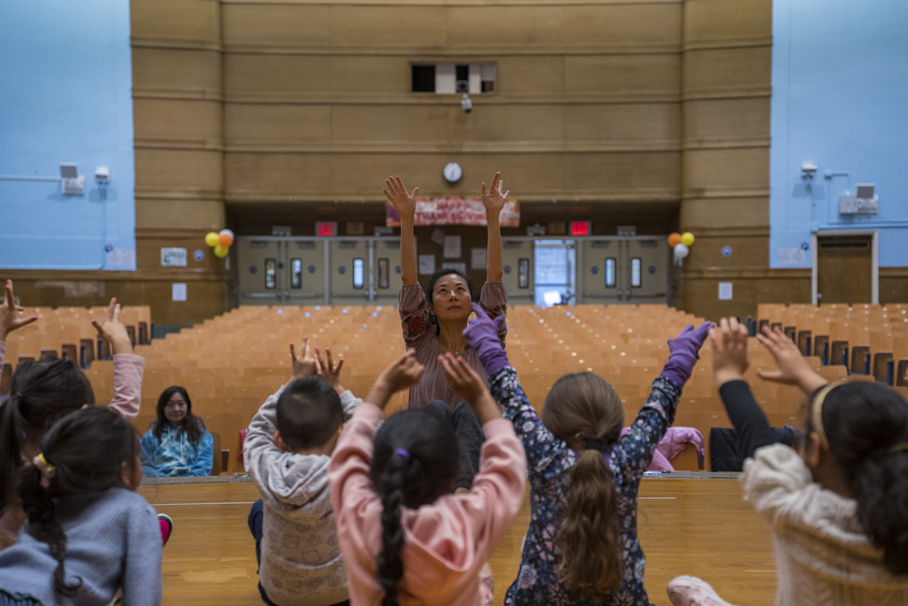 Tang raises her arms as children seated on the floor follow.