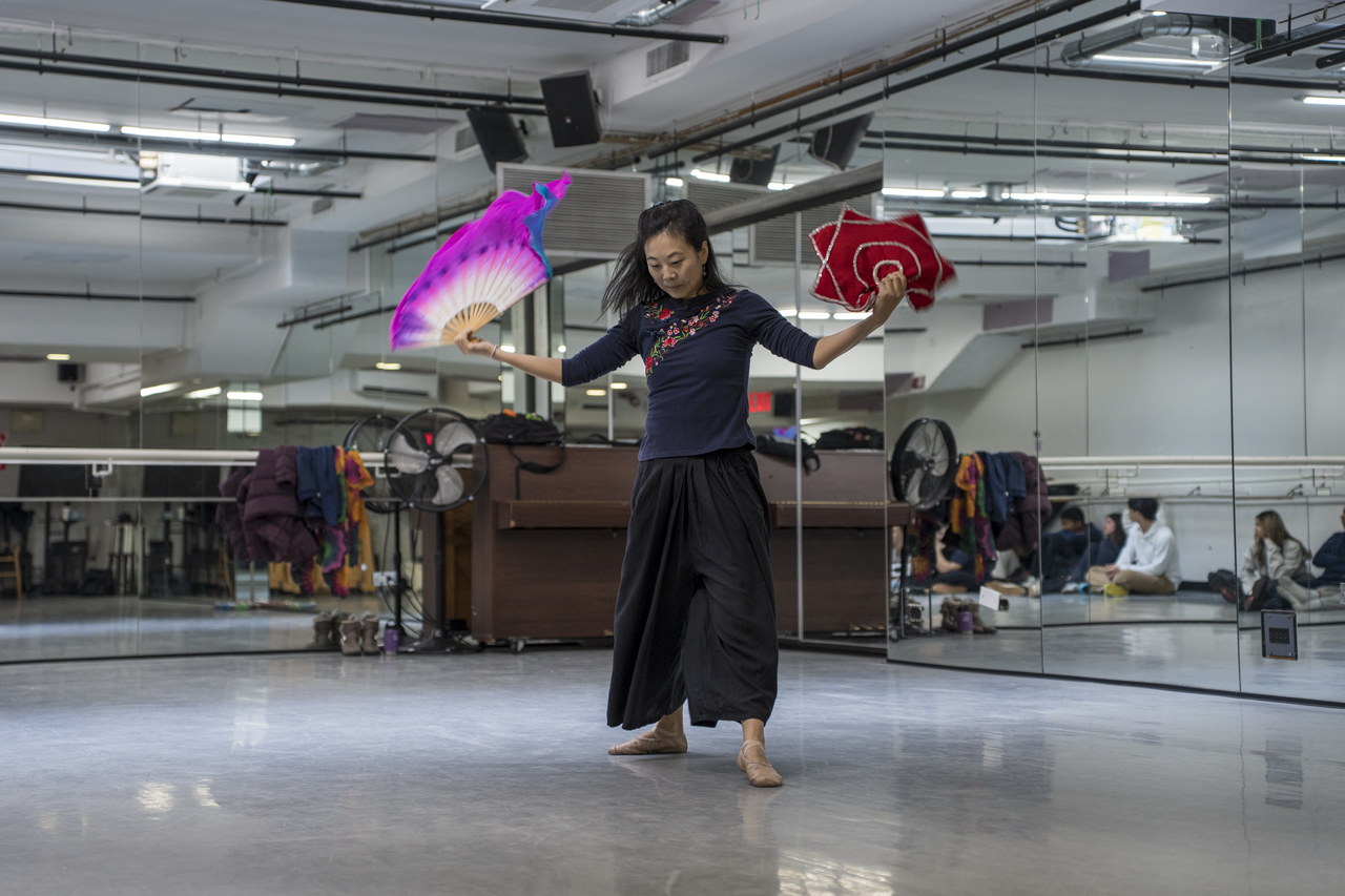 With a fan in each hand, Tang demonstrates as students and shadows fill the mirror.