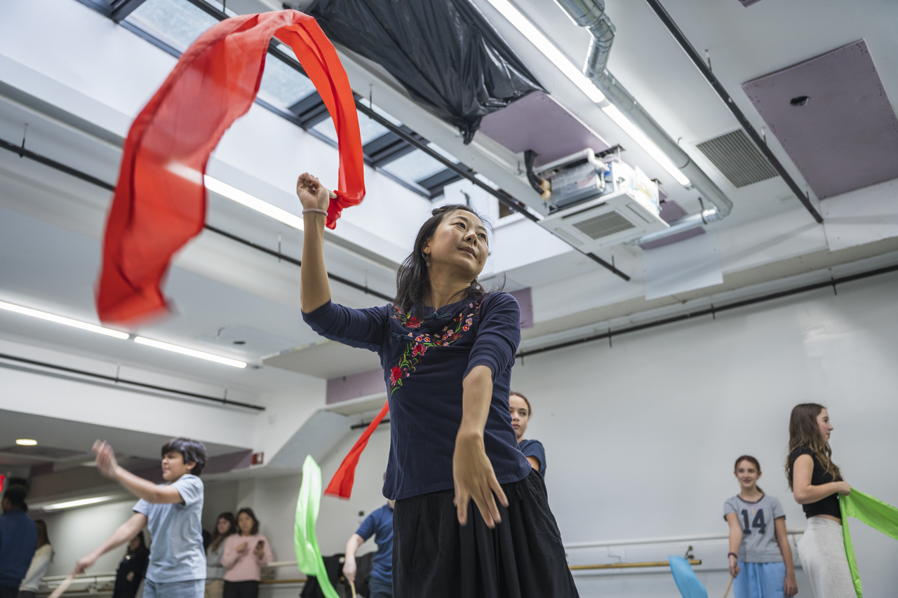 Tang leads with a red ribbon as students rehearse behind her.