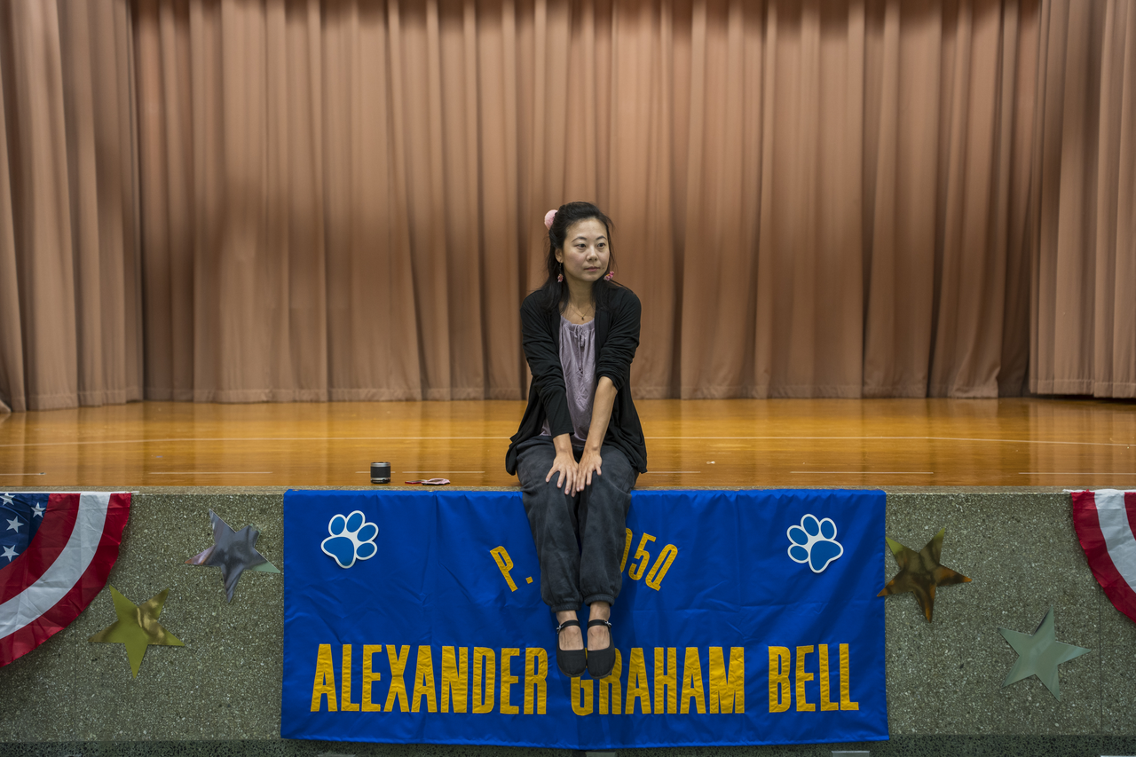 Between demonstrations, Tang rests on the edge of an empty auditorium stage.