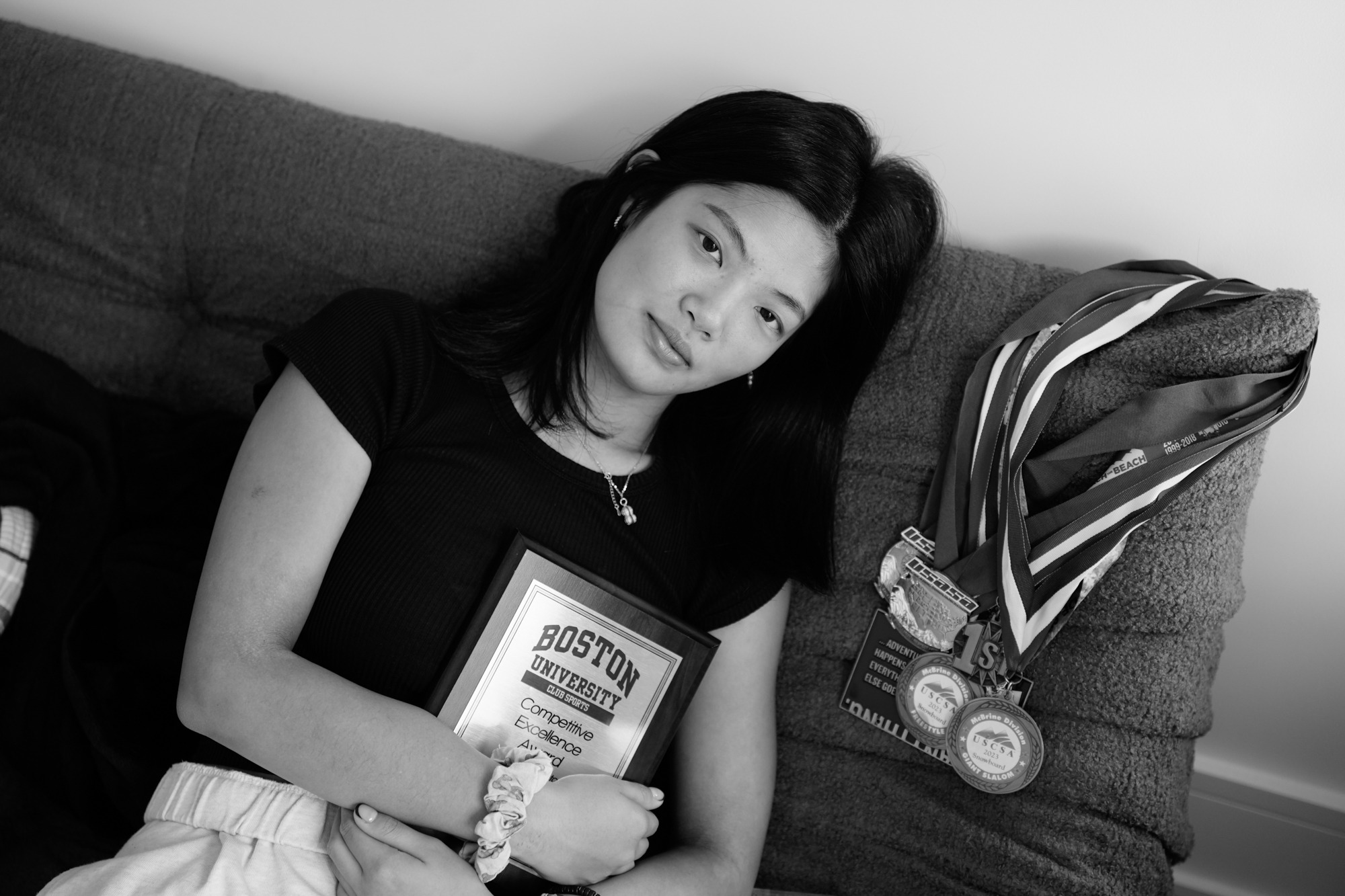 Rachel Zhong, 23, lies beside ski medals and certificates earned during her years at Boston University. New York, Nov. 22, 2025.