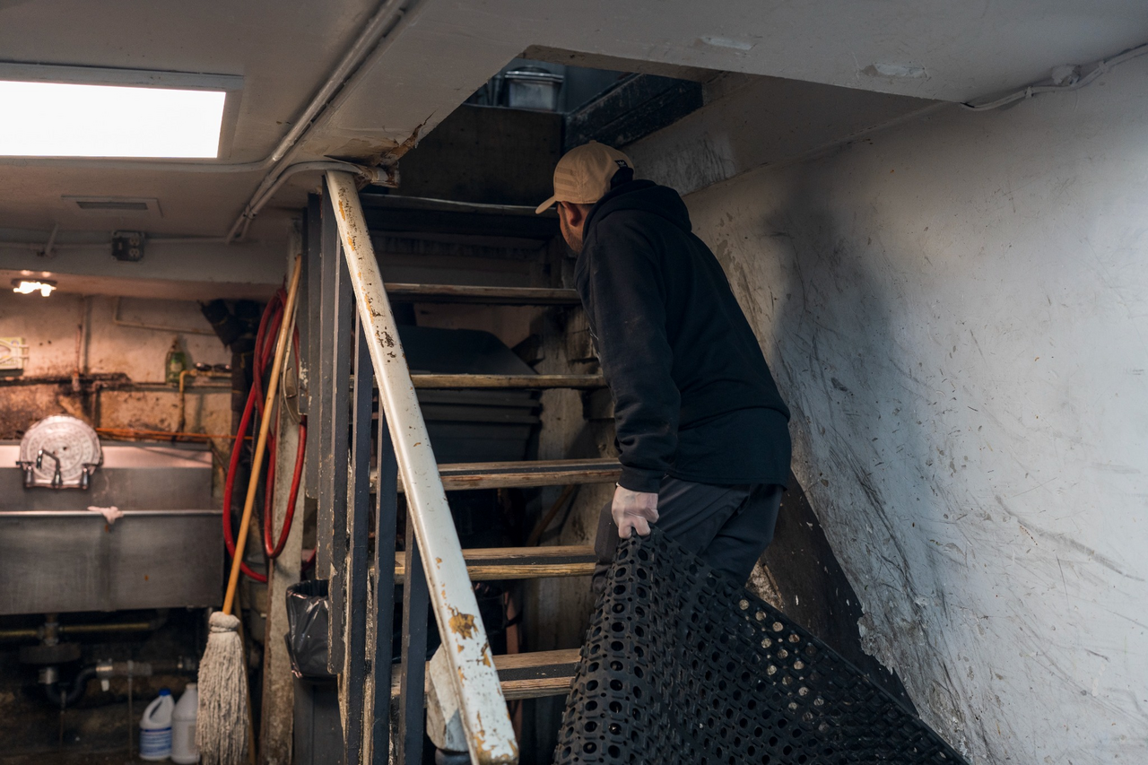 An employee carries a rubber floor mat on the narrow staircase between the basement and the kitchen.