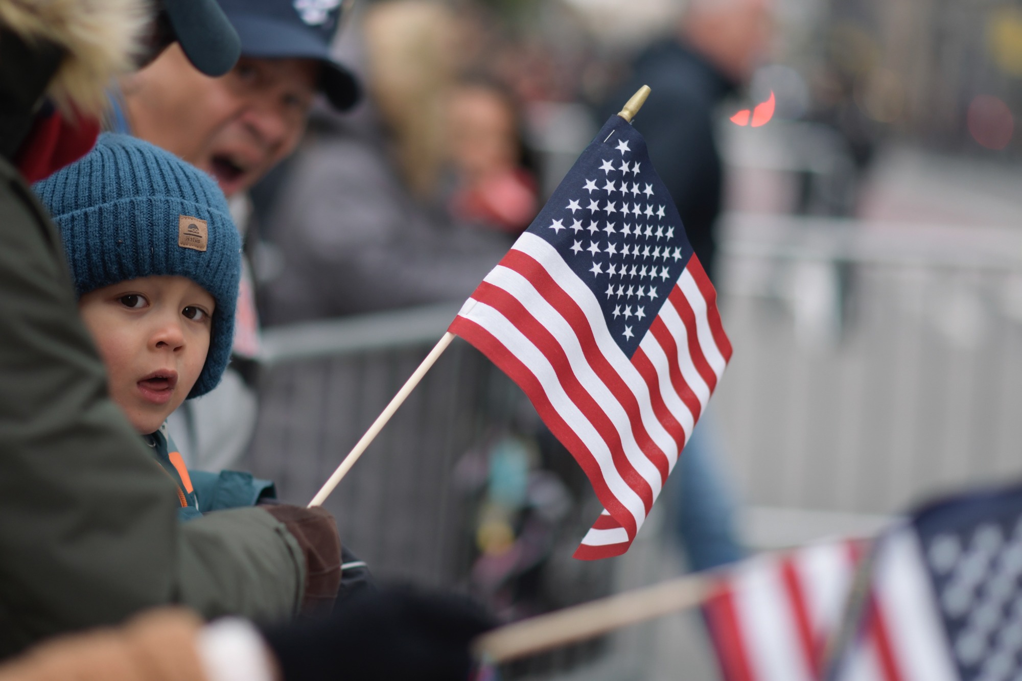 A child watches the parade while holding a small U.S. flag.