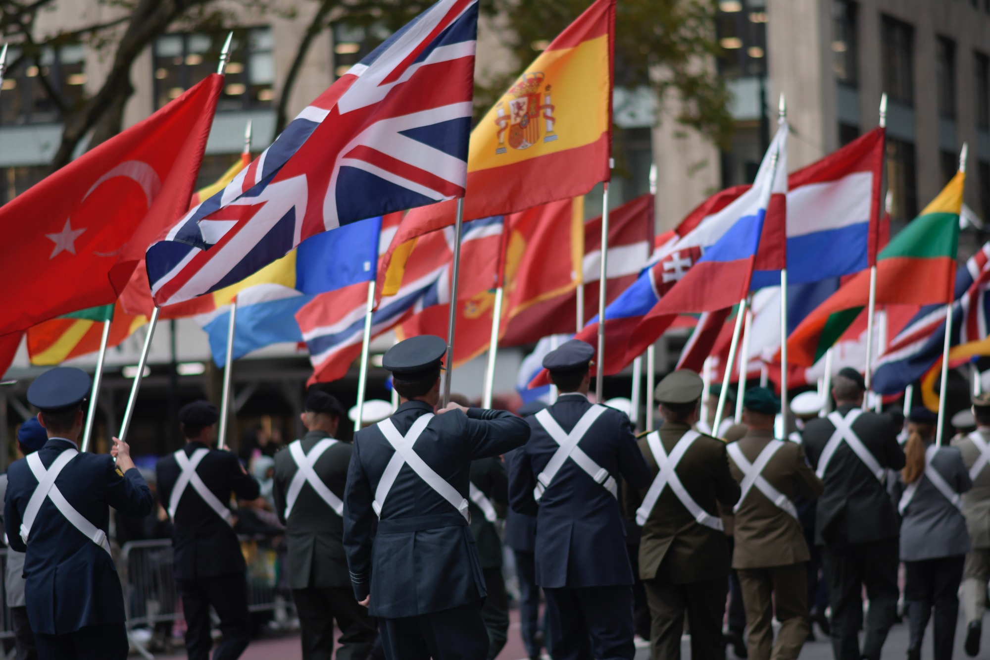 Service members march away beneath a field of international flags.