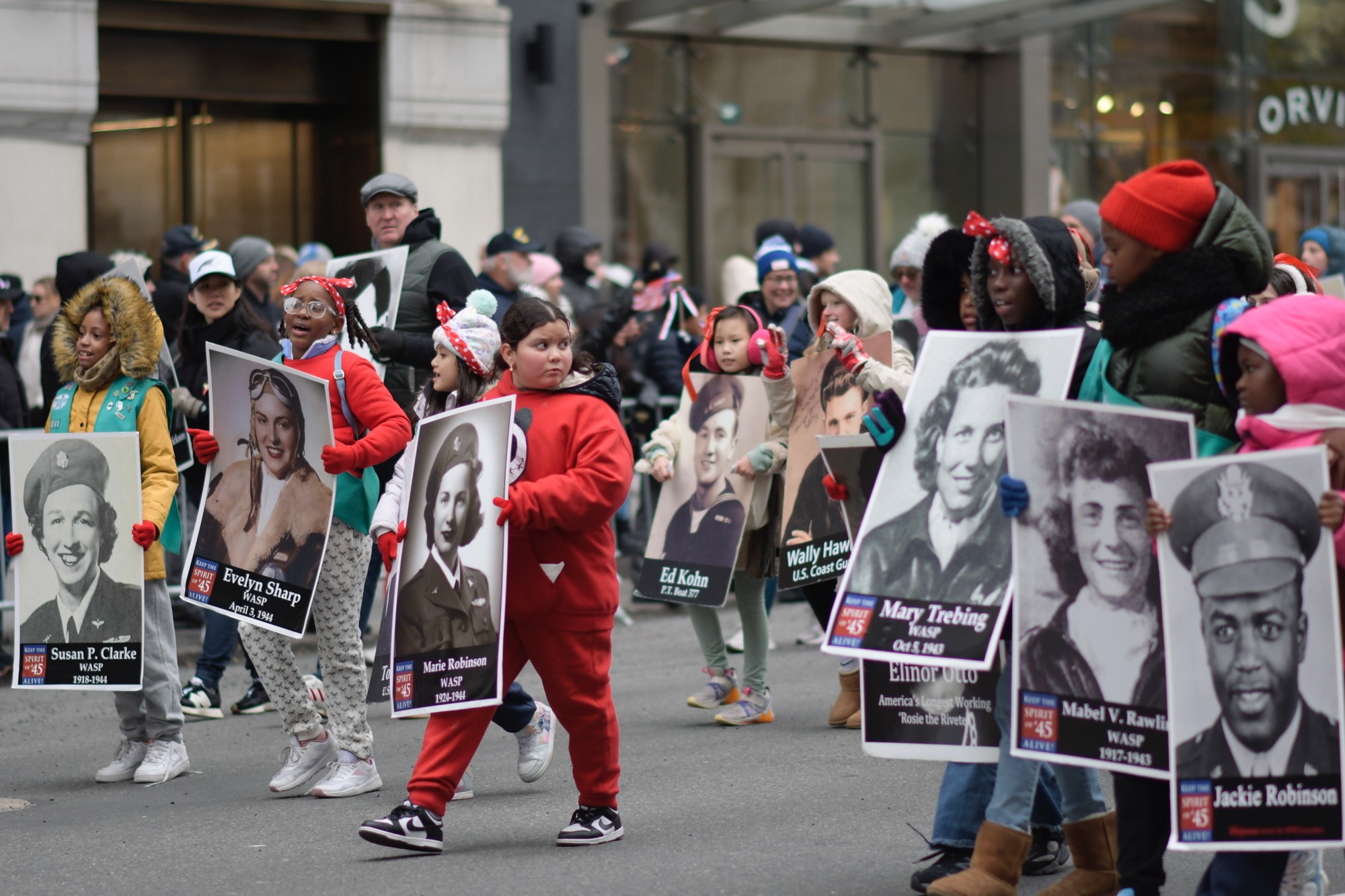 Children march with portraits honoring earlier generations of service members.